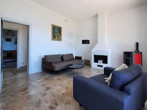 Una sala de estar con un sofá, una mesa de centro redonda, una chimenea y una cocina visible a través de una puerta abierta.