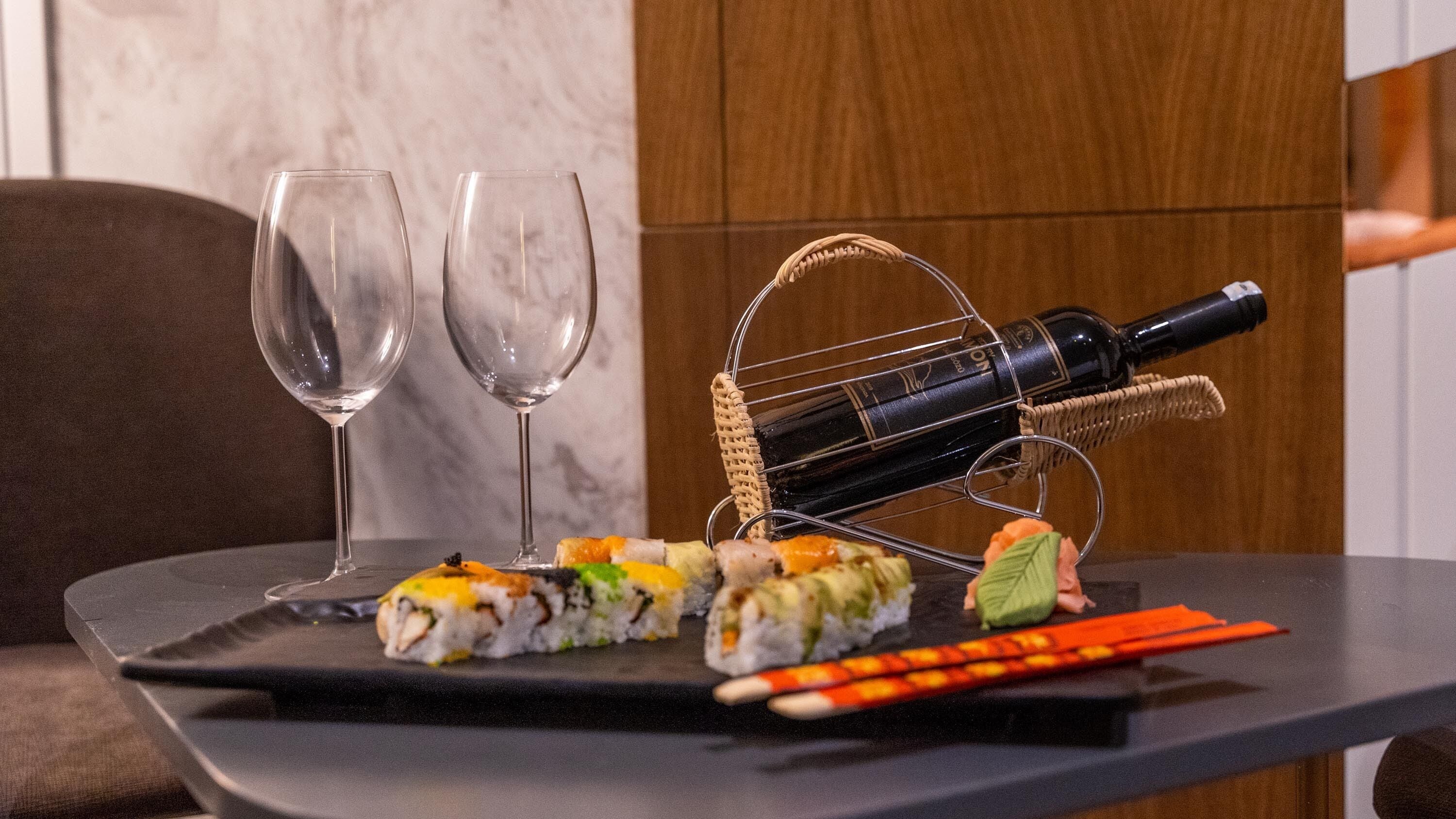 Una mesa con sushi, dos copas de vino vacías y una botella de vino sobre un posavasos.