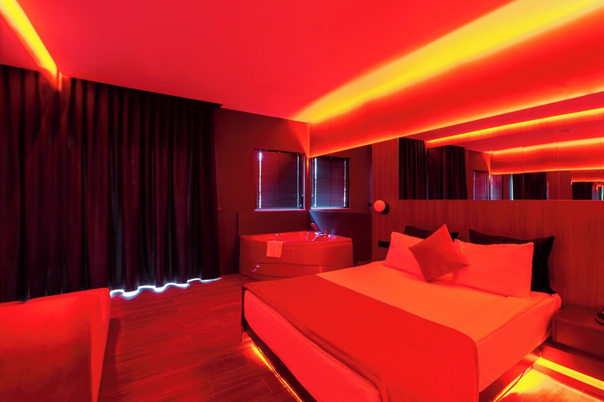 A room with a large bed, a nightstand, and a window with blinds.