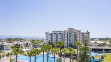 A hotel with a large pool, palm trees, and a view of mountains.