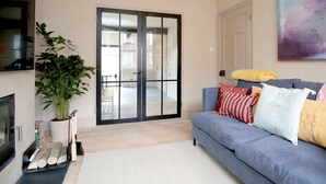 A modern living room with a blue sofa, a large potted plant, and a sliding glass door leading to a balcony. - Stunning, Brand New 3BR Home - Central Oxford - Pass the Keys (Oxford)