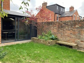 A modern house with a glass door entrance, a brick wall, and a small garden area with a bench and plants. - Stunning, Brand New 3BR Home - Central Oxford - Pass the Keys (Oxford)