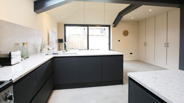A modern kitchen with a central island, black cabinetry, and a large window providing natural light. - Stunning, Brand New 3BR Home - Central Oxford - Pass the Keys (Oxford)