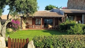 Een huis in mediterrane stijl, met een betegeld dak, een stenen muur en een verzorgde tuin.