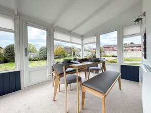 A conservatory with a dining table set for four, surrounded by chairs with grey cushions. - 3 bedroom accommodation in Balintore (Balintore)