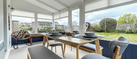 A conservatory with a dining table set for four, surrounded by cushioned seating.