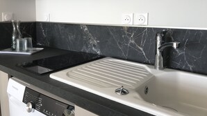 A modern kitchen with a black marble backsplash, a stainless steel sink, and a built-in dishwasher. - THE LAVOISIER TERRACE (La Rochelle)