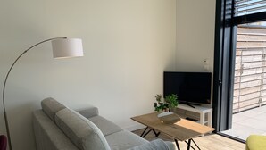 A modern living room with a grey sofa, a floor lamp, a wooden coffee table, and a TV on a white stand. - THE LAVOISIER TERRACE (La Rochelle)