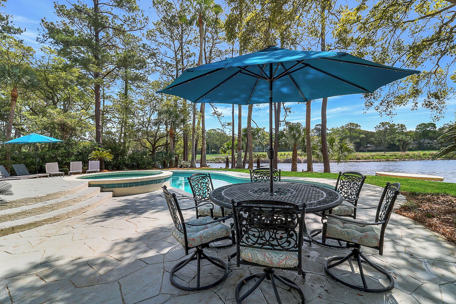 A patio with a pool, surrounded by trees and a view of a lake.