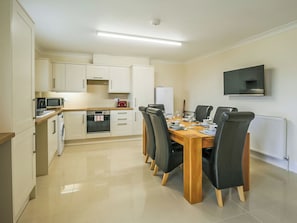 Una cocina moderna con armarios blancos, un microondas, una estufa y una mesa de comedor con sillas.