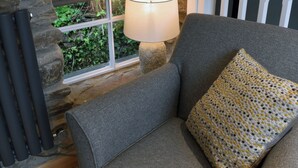 A cozy room with a grey sofa, a patterned pillow, a table lamp, and a stone wall.
