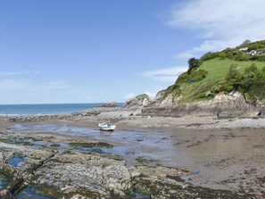 A rocky beach with a boat, cliffs, and a grassy hill.