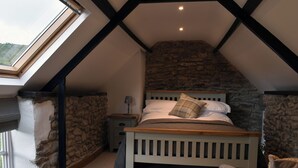 A bedroom with a sloped ceiling, stone walls, a wooden bed, a nightstand, and a window.