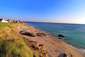 A coastal beach with rocky terrain and white buildings in the background.