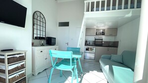 A compact living space with a kitchenette, a dining area with a turquoise chair, and a sofa.