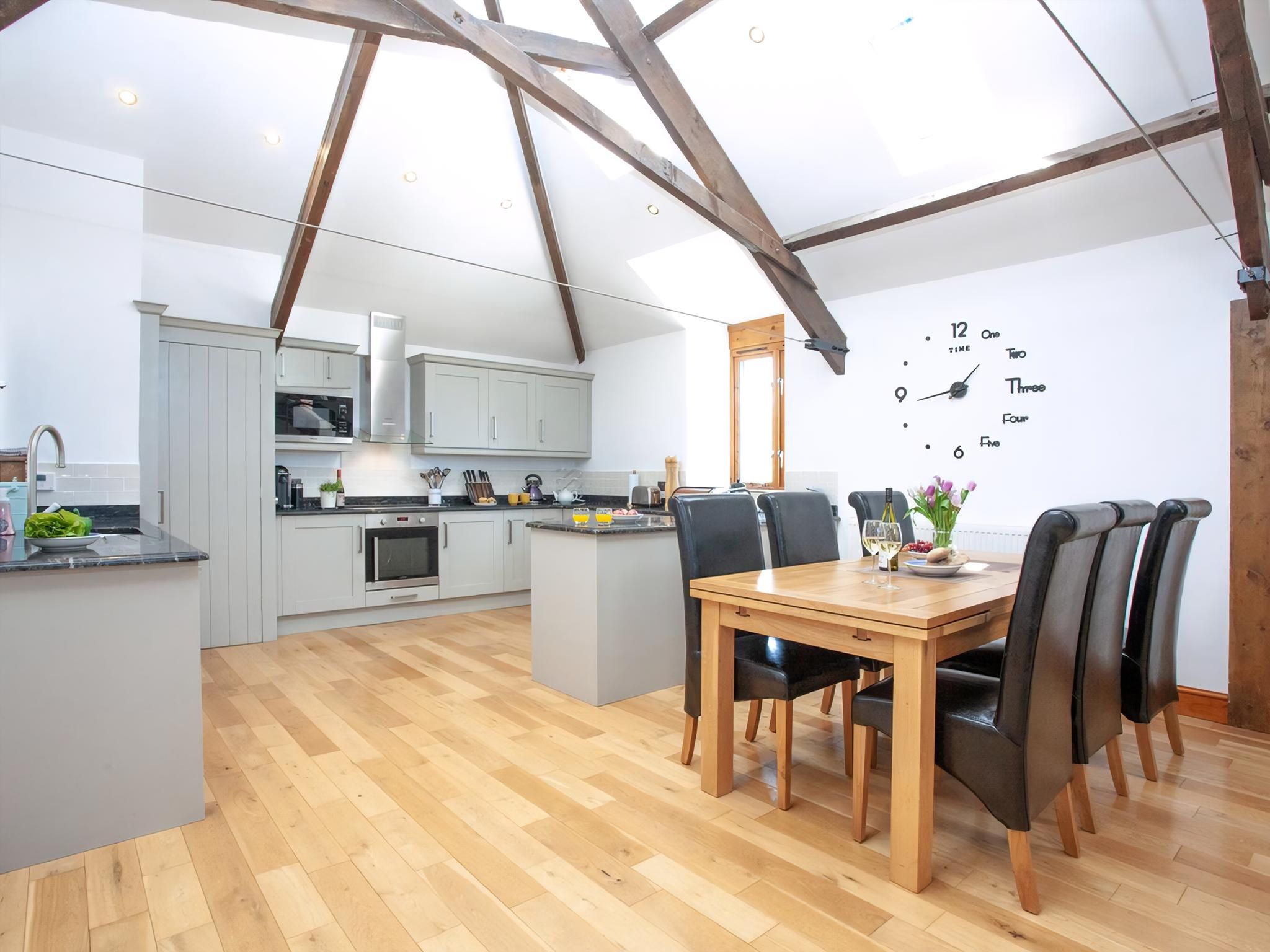 A modern kitchen with a dining area, wooden beams, and a clock on the wall.