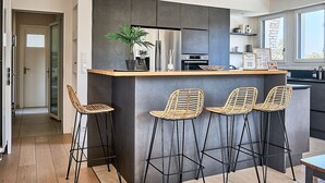 Una cocina moderna con una isla central, taburetes de bar y una planta en maceta.
