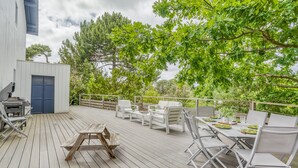 Una terraza de madera con mobiliario exterior, que incluye una mesa, sillas y una parrilla.