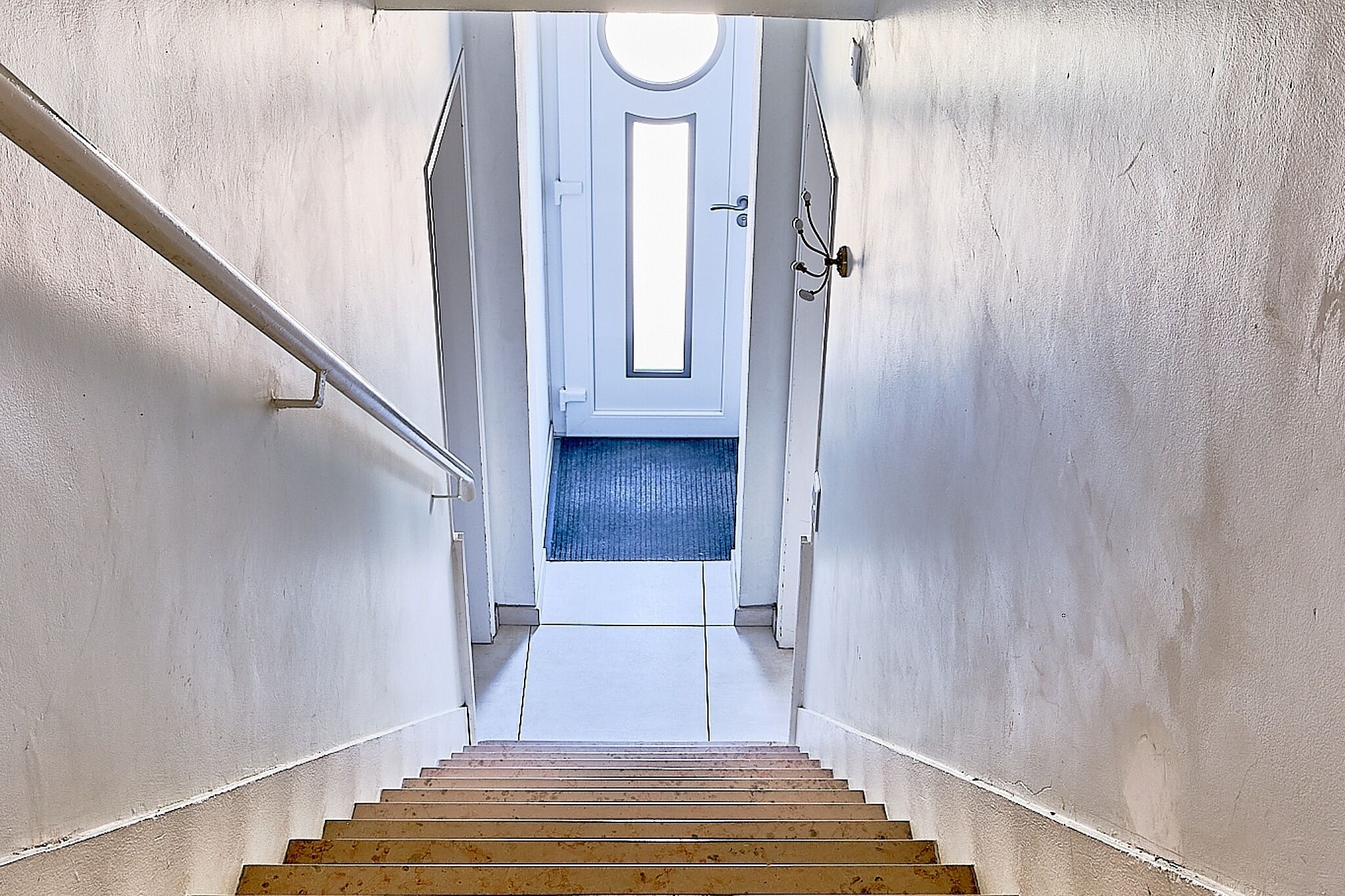 Eine Treppe führt zu einer Tür mit einem runden Fenster, weißen Wänden und einem blauen Teppich.