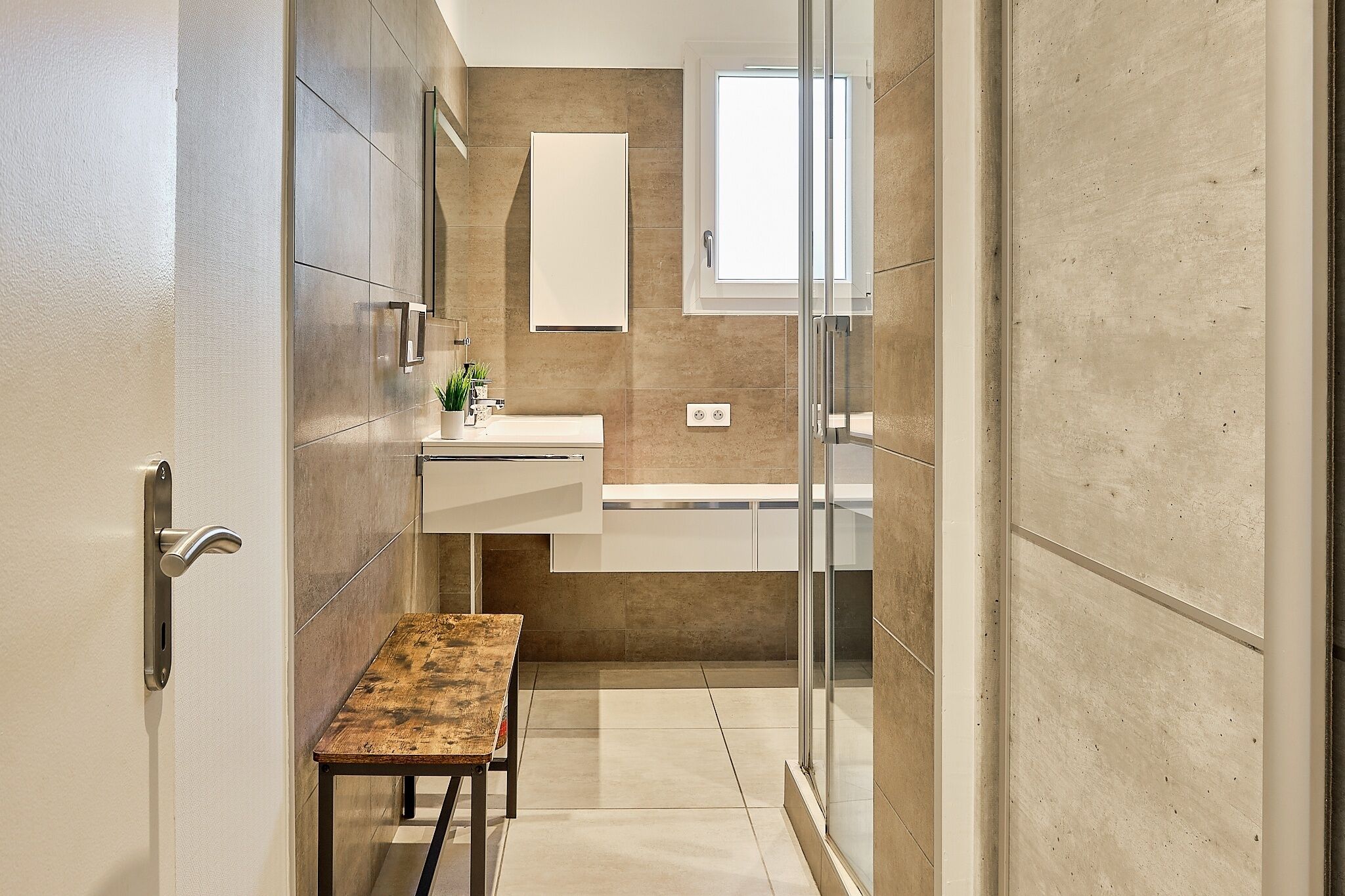 Un bagno moderno con cabina doccia in vetro, una panca in legno e un lavandino bianco.