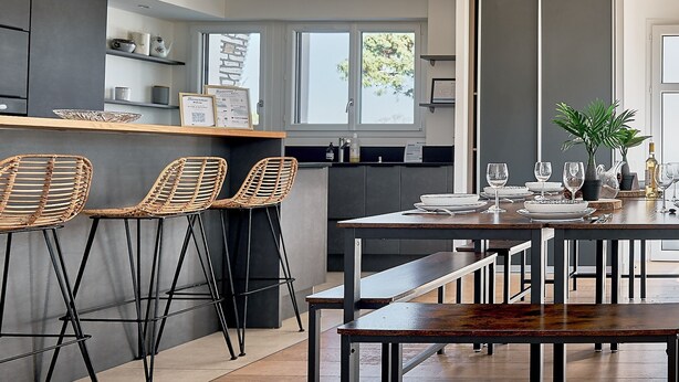 Una cocina moderna con barra, taburetes, una mesa de comedor con bancos y una planta en maceta.
