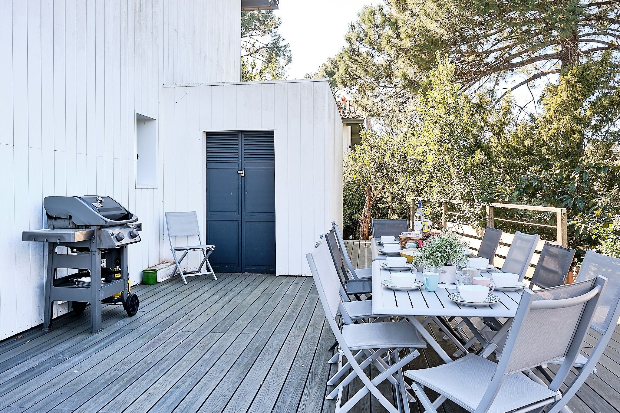 Eine Terrasse mit Grill, Esstisch, Stühlen und einer Tür.