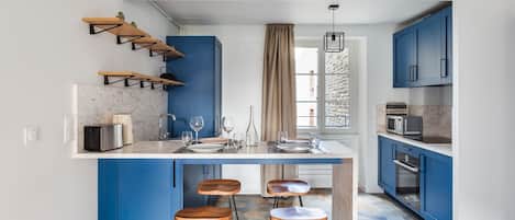 Una cocina moderna con armarios azules, encimera de mármol y una isla central con taburetes.