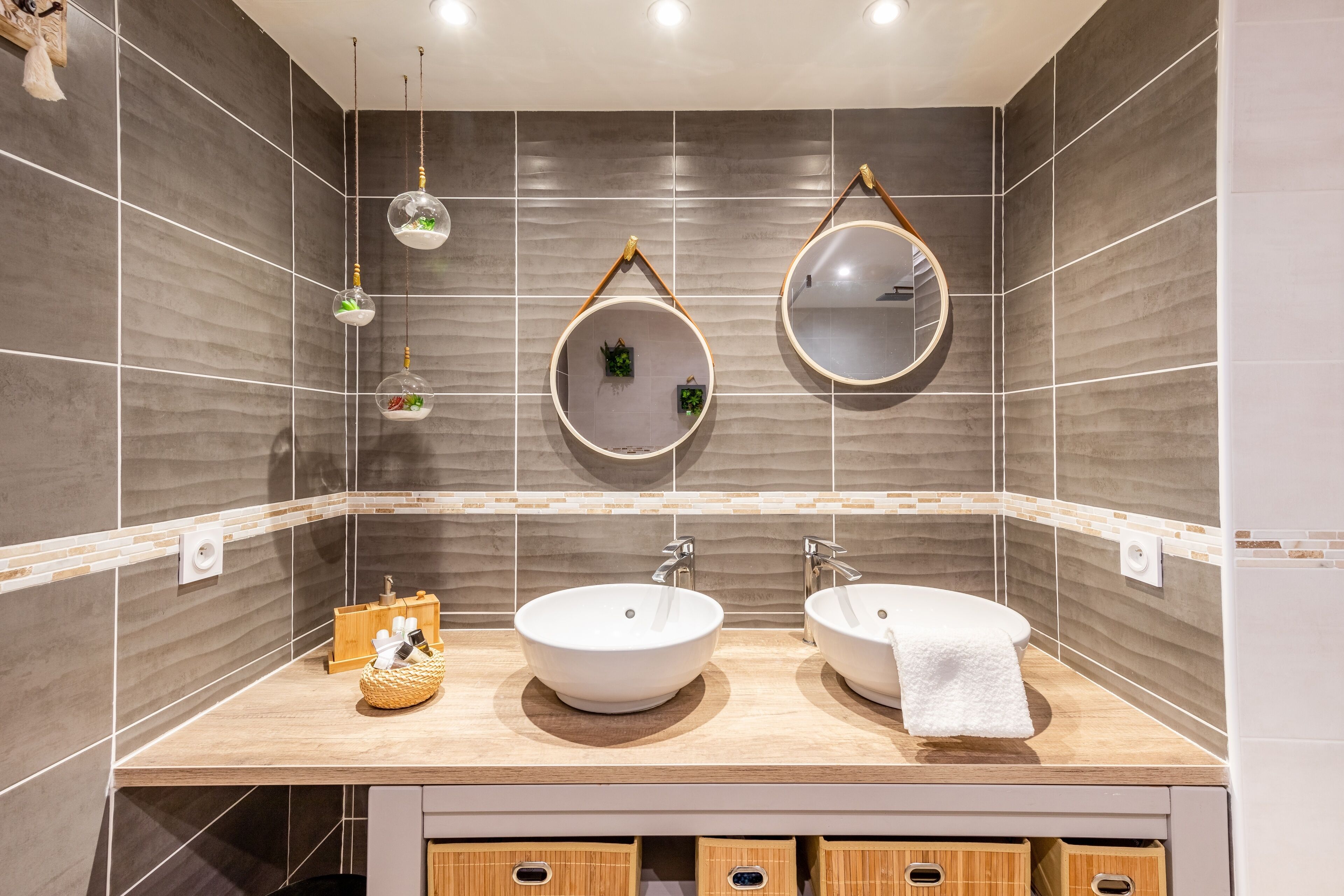 Une salle de bain moderne avec deux lavabos, un miroir et des luminaires décoratifs suspendus.