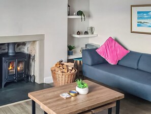 A living room with a wood-burning stove, a blue sofa with a pink pillow, a wooden coffee table, and a basket of firewood.
