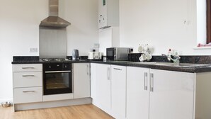 Una cucina moderna con mobili bianchi, una cappa aspirante in acciaio inossidabile, forno integrato, microonde e lavello con rubinetteria.