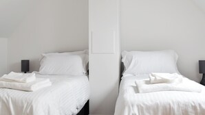 Camera d'albergo minimalista con due letti, lenzuola bianche e un design semplice e pulito.