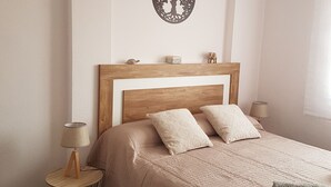 A bedroom with a wooden headboard, a round wall decoration, a bedside lamp, and a bed with patterned pillows.