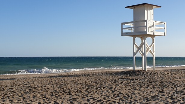 A lifeguard tower on a sandy beach with the ocean in the background.