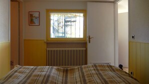 A bedroom with a bed, a radiator, a window with bars, and a door. - Casa Cannobio Carmine (Carmine)