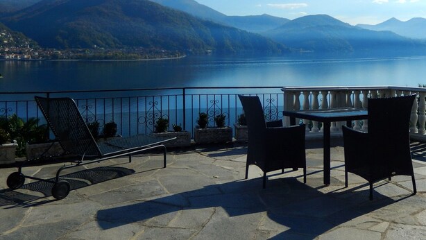 A terrace with a table and chairs overlooking a lake with mountains in the background. - Casa Cannobio Carmine (Carmine)