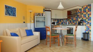 A compact living space with a sofa, chairs, a dining table, a kitchen area with a microwave, and a colorful tiled backsplash. - Casa Cannobio Carmine (Carmine)