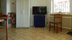 A room with a white wardrobe, a blue cabinet, a television, a window with a view, a radiator, and a chair. - Casa Cannobio Carmine (Carmine)