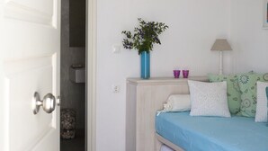Una camera da letto con un letto, un comodino, una lampada, un vaso con fiori e una porta che dà su un'altra stanza.