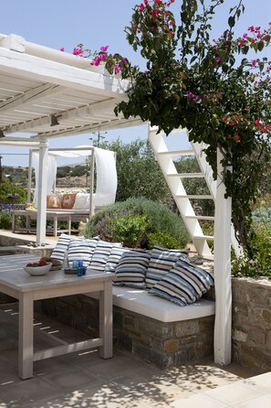 A covered outdoor seating area with a white pergola, stone walls, and a view of the landscape.
