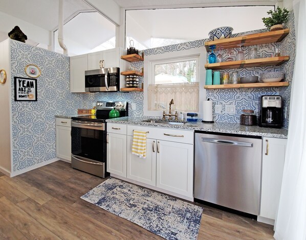 A modern kitchen with white cabinets, stainless steel appliances, and patterned backsplash. - Green Heron Cottage (Sherrills Ford)