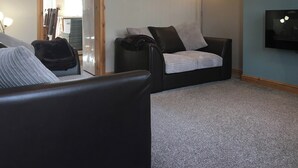 Ein Wohnzimmer mit einer Couch, einem Couchtisch und einer Lampe. Eine Tür führt in einen anderen Raum, und ein Gemälde hängt an der Wand.