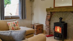 Una sala de estar acogedora con chimenea, un sofá, un cofre de madera y una ventana con cortinas.