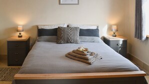 Una cama bien hecha con ropa de cama a rayas, dos mesitas de noche con lámparas, una obra de arte enmarcada en la pared y una ventana con cortinas.