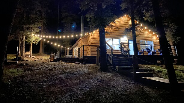 A wooden cabin with a porch, string lights, and a staircase leading to the entrance.