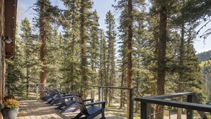 A wooden deck with lounge chairs and a railing overlooking a forest.