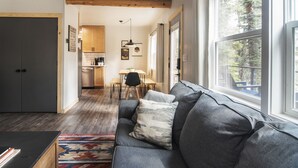 A modern living room with a gray sofa, a patterned throw pillow, and a view of a dining area with a wooden table and chairs.