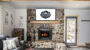A cozy living room with a stone fireplace, a mounted sign above it, a gray sofa, and a coffee table with a book.