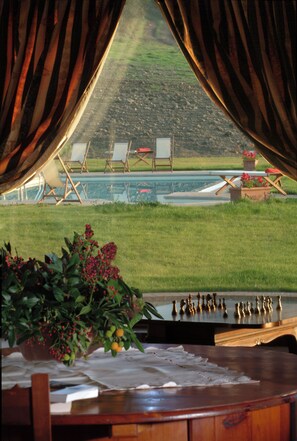 A room with a view of a pool, outdoor chairs, and a table with chess pieces.