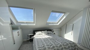 Een slaapkamer met dakraam, een bed met een bedovertrek met patroon, een nachtkastje met lamp en een kledingkast.