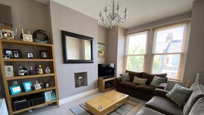 Een woonkamer met een bank, salontafel, televisie, boekenkast en een open haard.